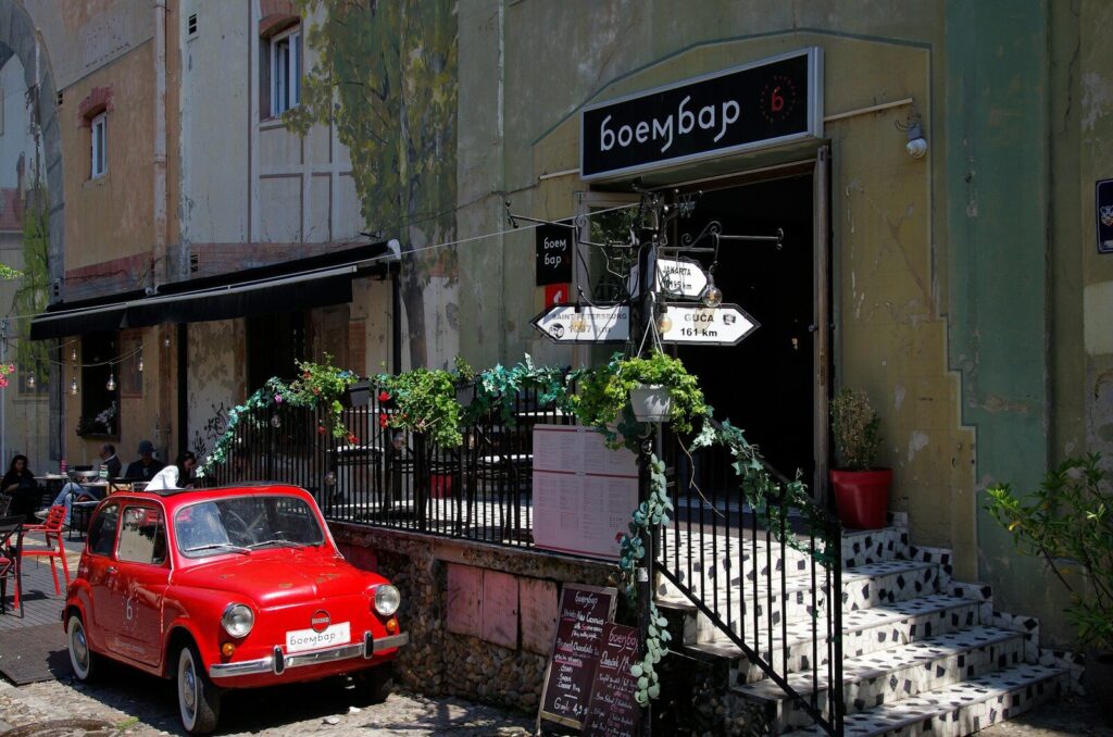 Red car parked outside a bar with plants.
